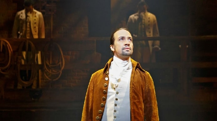 Lin-Manuel Miranda in his white shirt and brown coat while performing for Hamilton show